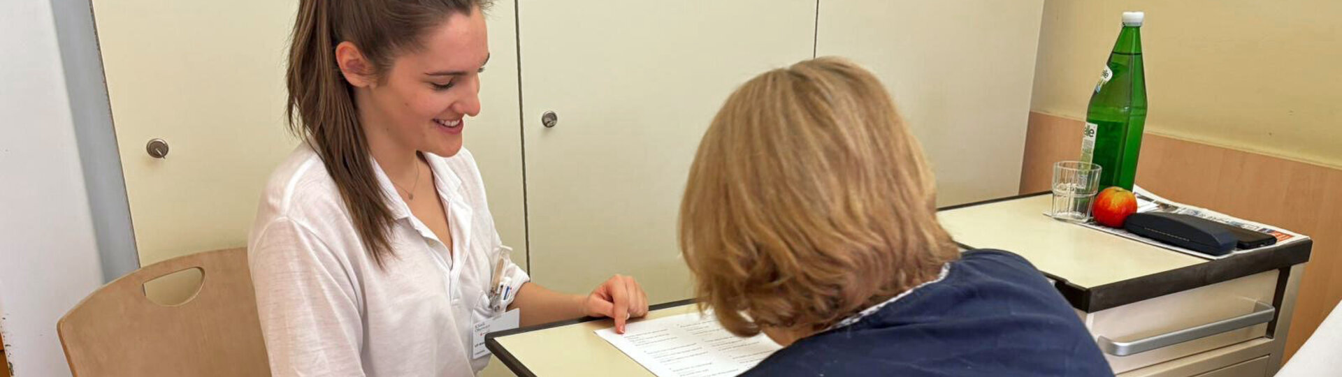 Eine Therapeutin zeigt einer Patientin etwas auf einem Blatt, die Patientin ist nur von hinten zu sehen, beide sitzen