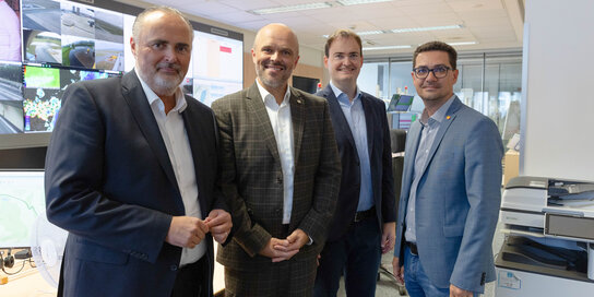 Vier Männer in einem Gruppenbild vor Bildschirmen