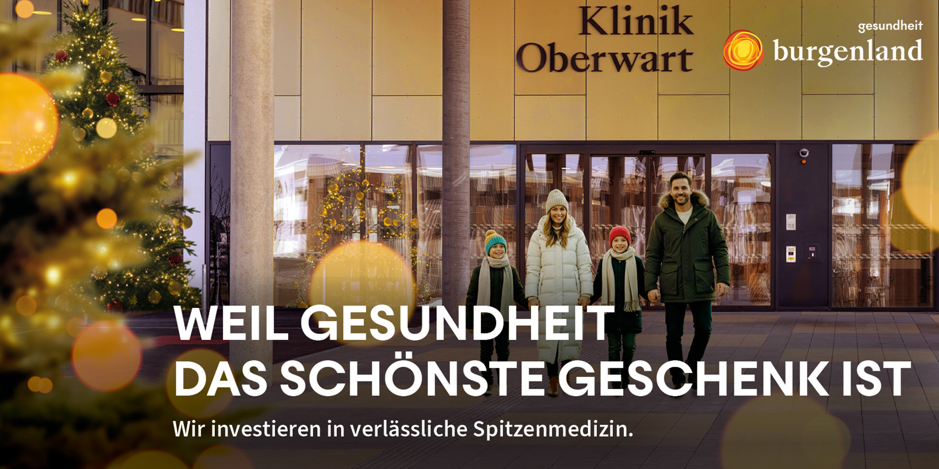 Eingang der Klinik Oberwart in weihnachtlicher Beleuchtung inklusive Baum und einer jungen Familie, Vater, Mutter, zwei Kinder