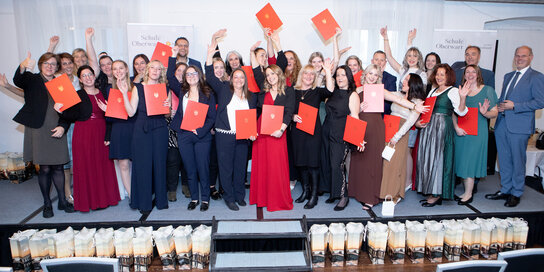 Eine sehr große Gruppe von Menschen bei einer Diplomverleihung zeigt ihre Diplome