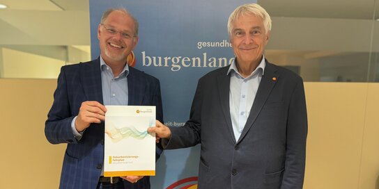 Zwei männliche Personen im Anzug stehen nebeneinander, einer hält einen Umweltbericht in der Hand