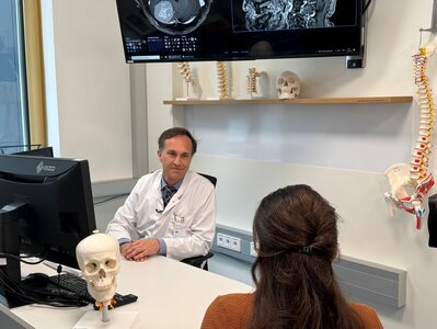 Ein Arzt in weißem Kittel sitzt an einem Tisch und berät eine Patientin