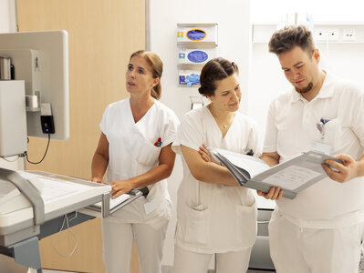 Drei Personen im Krankenhaussetting in weißer Kleidung