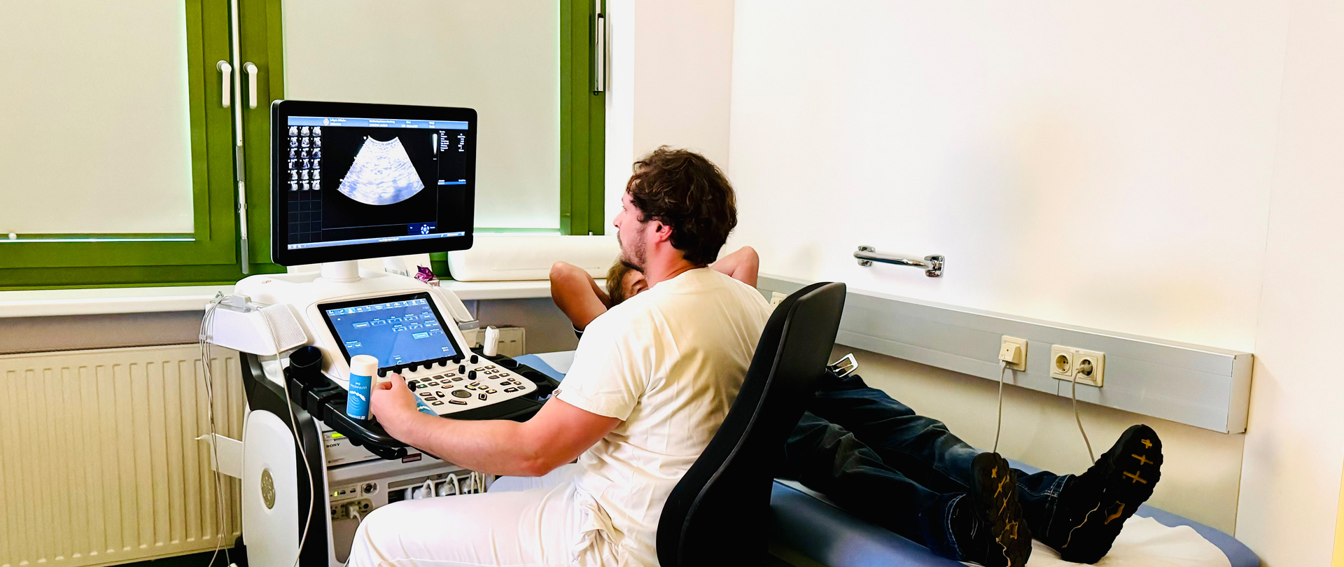 Ein Arzt sitzt an einem Ultraschallgerät samt Bildschirm und macht eine Untersuchung an einem Patienten