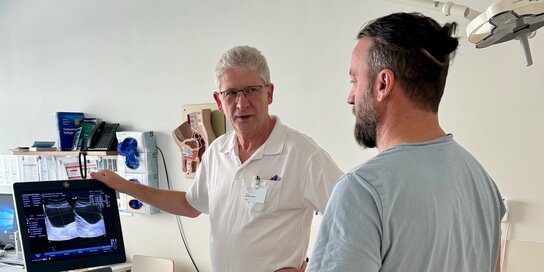 Ein Arzt und ein Patient bei einer urologischen Untersuchung, am Bild auch ein Monitor