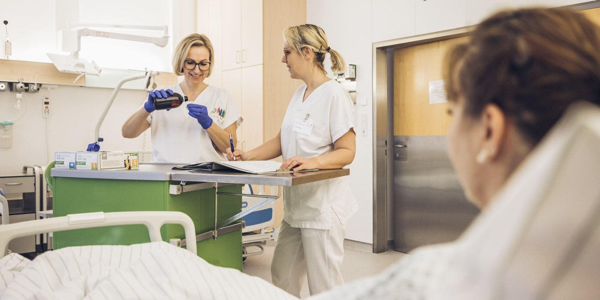 Foto: Gesundheit Burgenland Eine Frau liegt in einem Patientenbett, gegenüber stehen zwei Frauen in Weiß