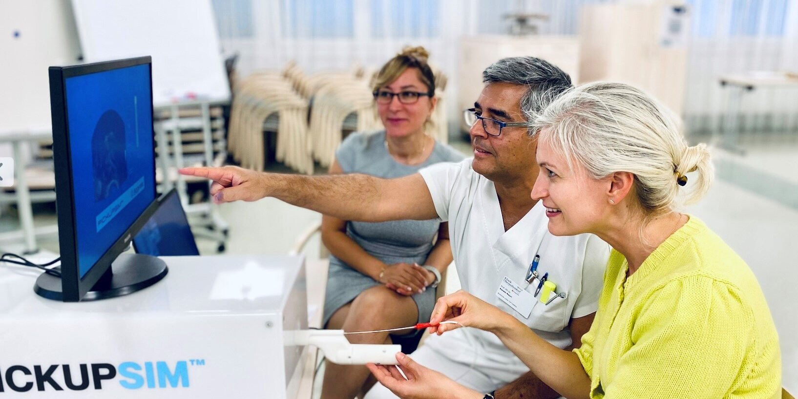 Drei Personen sitzen vor einem Bildschirm, einer zeigt auf etwas 