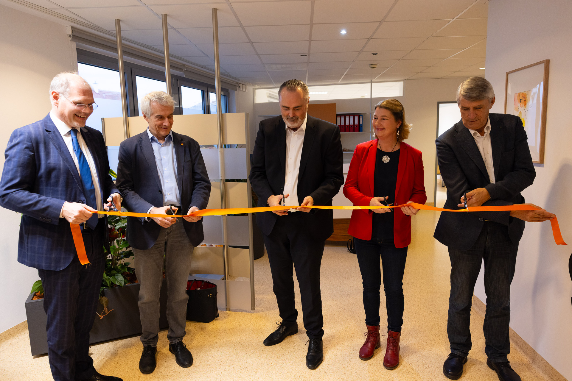 Sechs Personen stehen in einer Praxis und schneiden ein rotes Band zur Eröffnung durch