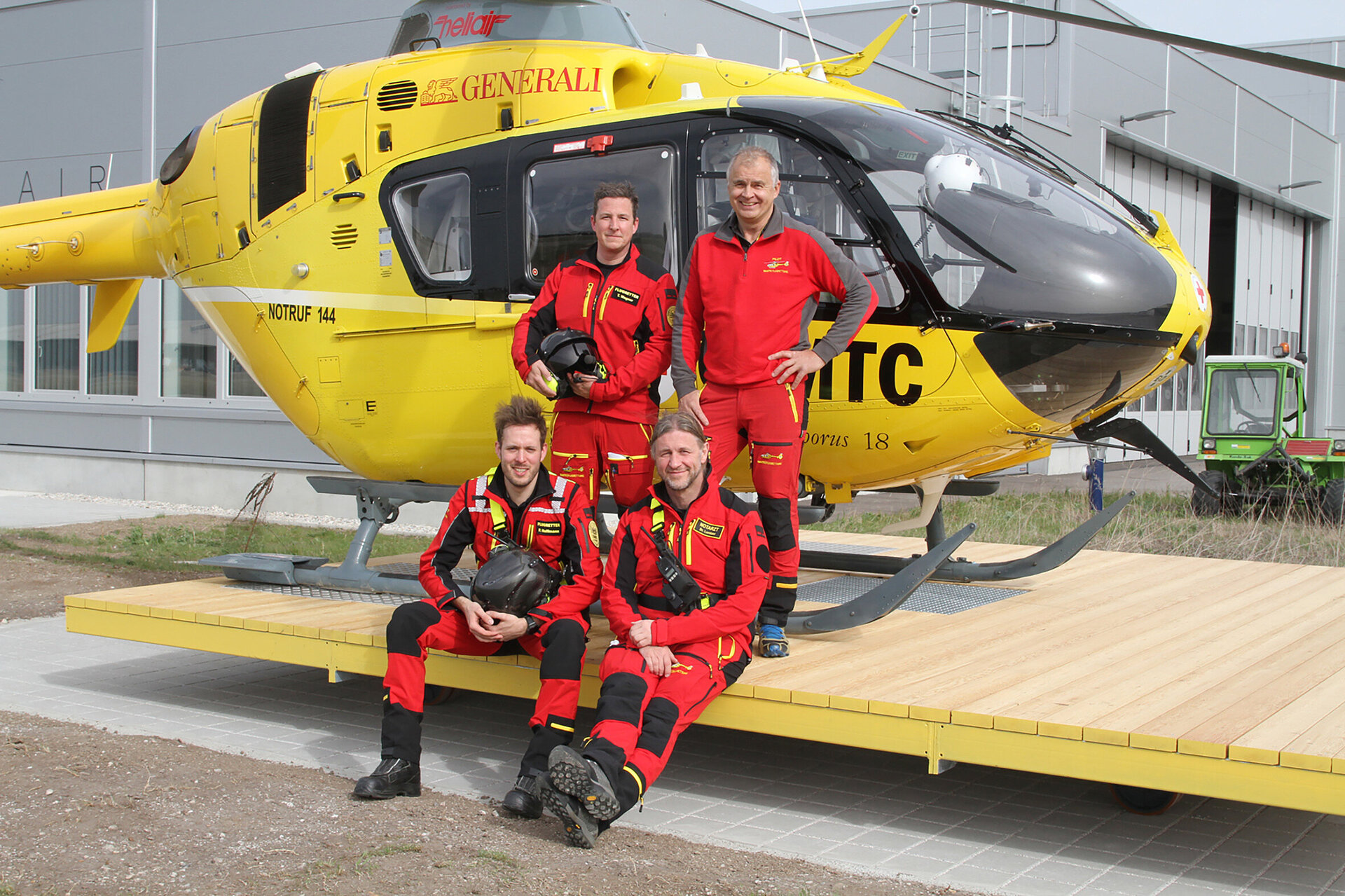 Foto: ÖAMTC ÖAMTC: gelber Hubschrauber mit Team (4 Personen in roter Arbeitskleidung)