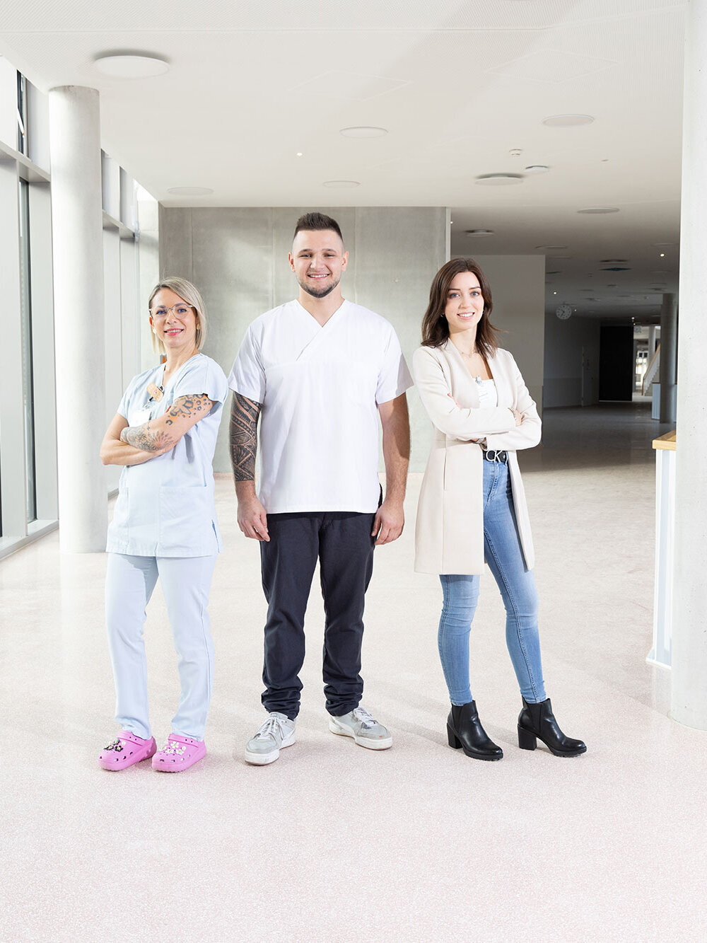 Karriere/Ausbildung: drei Personen in unterschiedlicher Arbeitskleidung auf Klinikflur