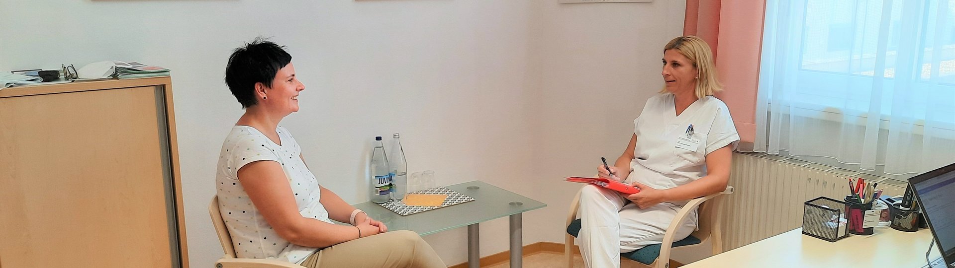 Zwei Frauen sitzen einander an einem Tisch gegenüber, die eine schreibt etwas 