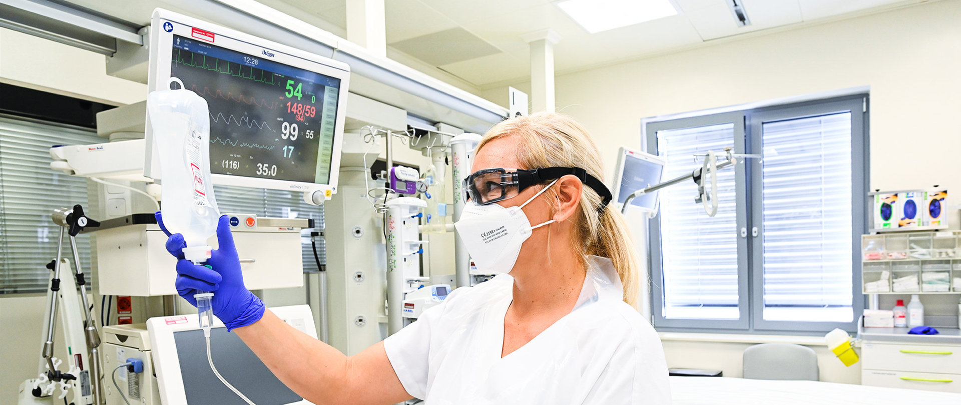 Eine Frau mit Maske und Schutzbrille in Weiß hält eine Infusion